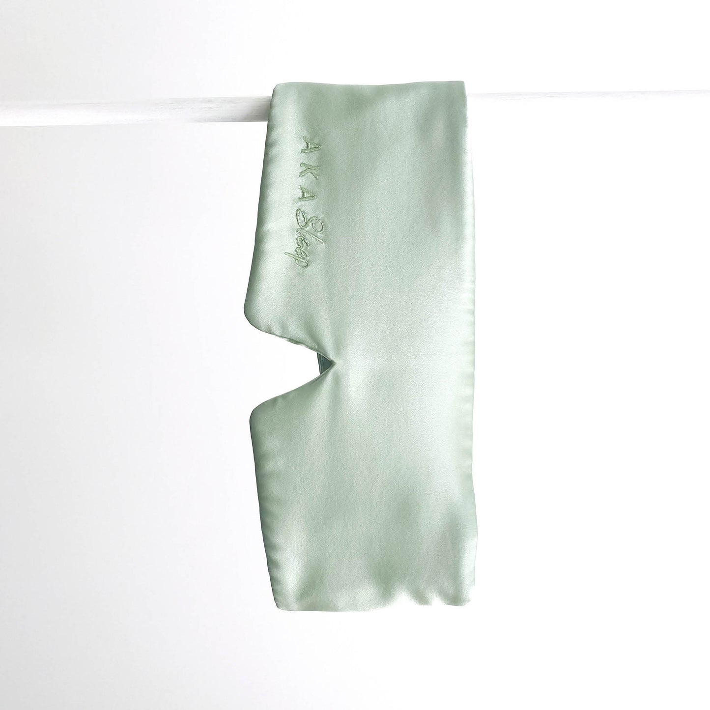 Sage green 100% Mulberry Silk AKA Sleep Deep Sleep Eye Mask hanging on a white rod in front of a white background