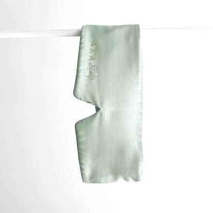 Sage green 100% Mulberry Silk AKA Sleep Deep Sleep Eye Mask hanging on a white rod in front of a white background